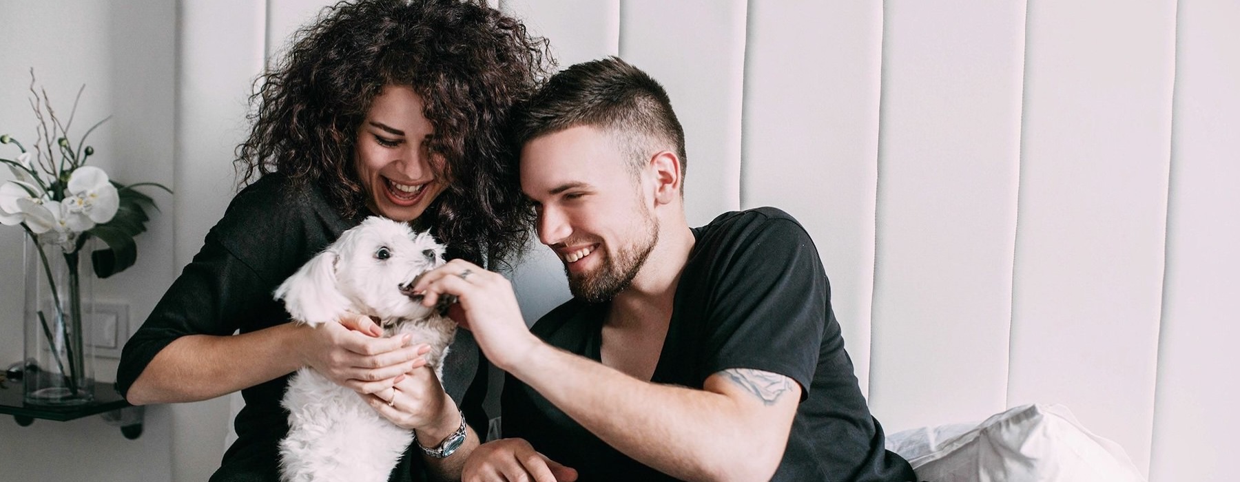 a man and woman sitting on a bed playing with a dog